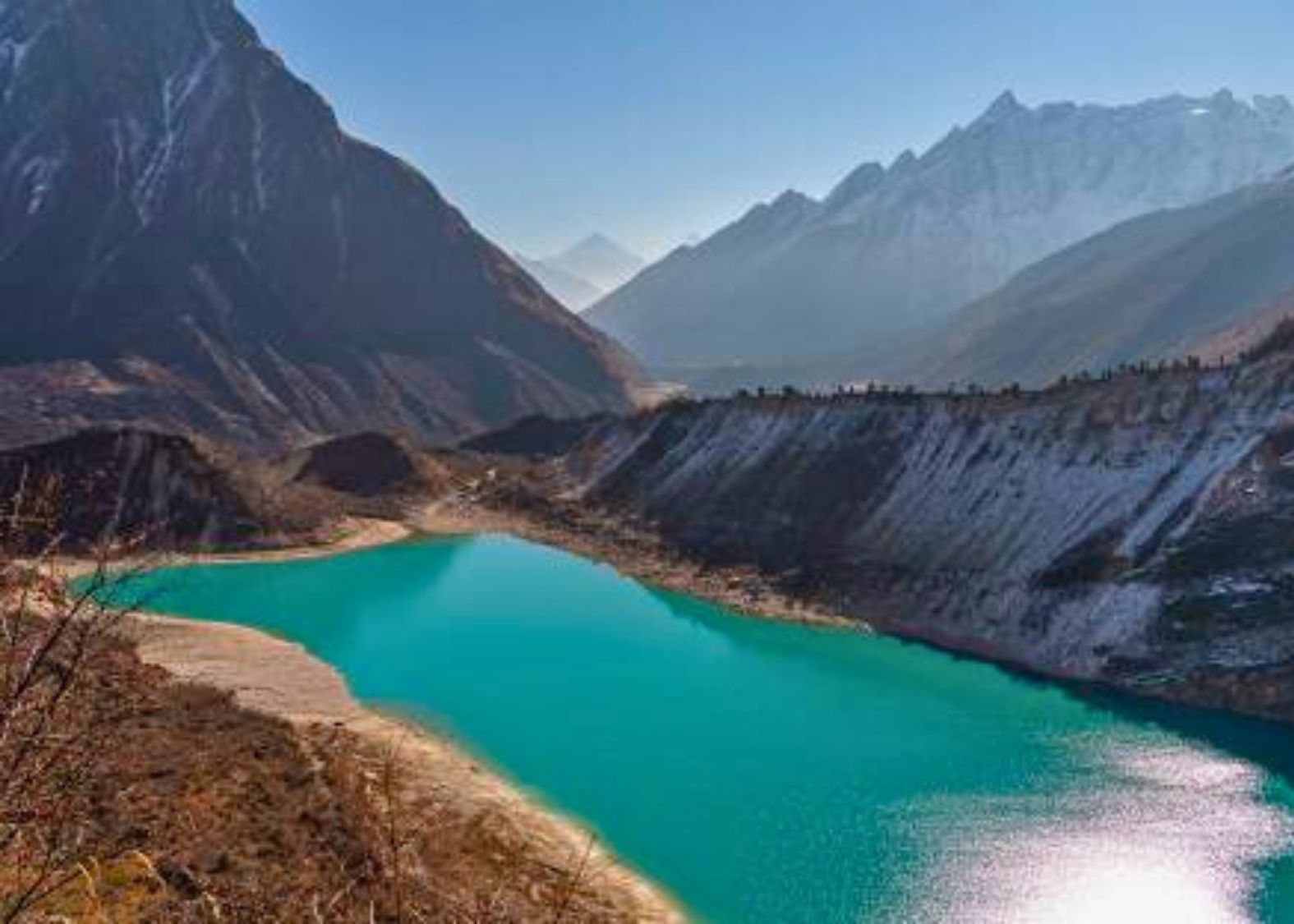 A clear day at Birendra Lake, showing the turquoise water and the surrounding rocky moraine landscape.